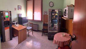 Una habitación de hotel compacta con kitchenette, refrigerador, microondas, máquina expendedora, televisor y una pequeña mesa con mantel.