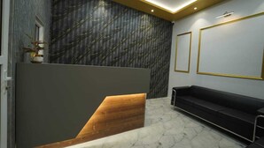 A reception area with a wooden reception desk, a black sofa, and a patterned wall. - Brij Hari Villa (Varanasi)