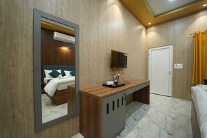 Ein Hotelzimmer mit einer Holzwand, einem Bett mit grün-weißer Bettwäsche, einem Holztisch mit Fernseher und einer weißen Tür.