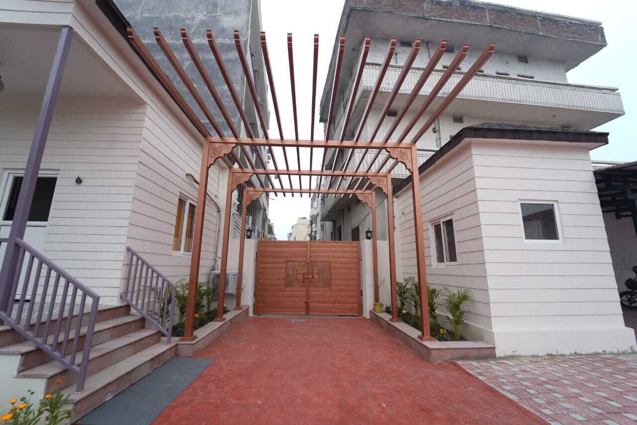 A gated entrance with a wooden pergola, a staircase, and a red carpet leading to a building with white siding.