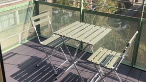Eine Dachterrasse mit grüner Metallreling, einem Sicherheitsnetz und zwei Metallstühlen.