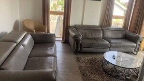 Ein Wohnzimmer mit zwei braunen Ledersofas, einem Glastisch und einem beigefarbenen Sessel.