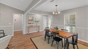 A dining area with a wooden table and chairs, a chandelier, and a window with blinds. - Renovated 3 Bed 2 Bath,Dog Friendly, Game Room, Fenced Yard, Well Equipped Kitchen, 5 Smart TVs (Dothan)