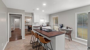 A modern kitchen with a central island, bar stools, and a dining area with a table and chairs. - Renovated 3 Bed 2 Bath,Dog Friendly, Game Room, Fenced Yard, Well Equipped Kitchen, 5 Smart TVs (Dothan)