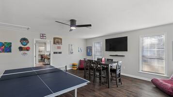 A modern living room with a ping pong table, dining area, and a flat-screen TV.