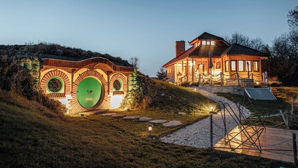 Una casa con un diseño circular único en la ventana, una puerta verde y un exterior bien iluminado al anochecer.