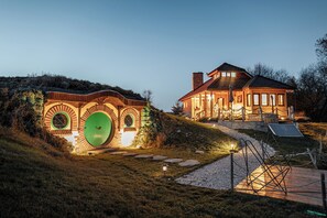 A house with a unique circular window design, a green door, and a well-lit exterior at dusk. - Enchanting Villa near lake with outside HotTub (Râșnov)