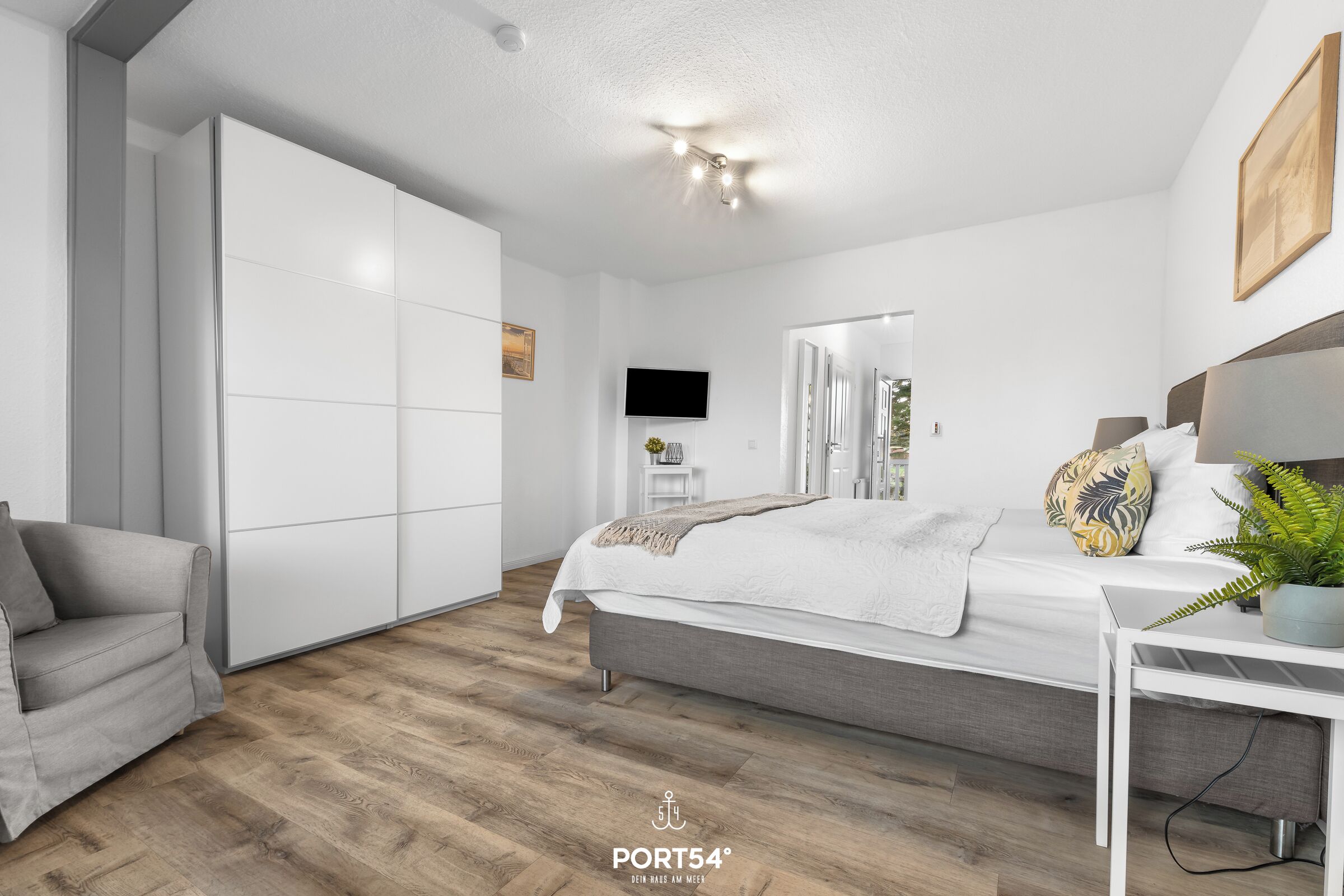 Un dormitorio moderno con cama, sofá gris, televisor y armario.