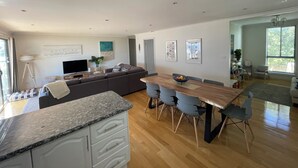 A modern kitchen with a wooden dining table and chairs, a built-in oven, and a large window providing natural light.