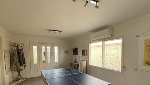A room with a ping pong table, a coat rack, and a window with blinds.