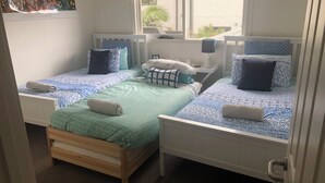 A room with two single beds, each with patterned bedding and pillows, a wooden bench, a nightstand with a lamp, and a Star Wars poster on the wall.