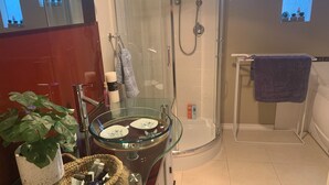 A modern bathroom with a glass shower enclosure, a glass sink with toiletries, and a potted plant.