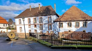 A historic building with a white facade and a red-tiled roof, featuring a central courtyard and a black metal fence. - Les gîtes de Wissembourg- Color Lodge (Wissembourg)