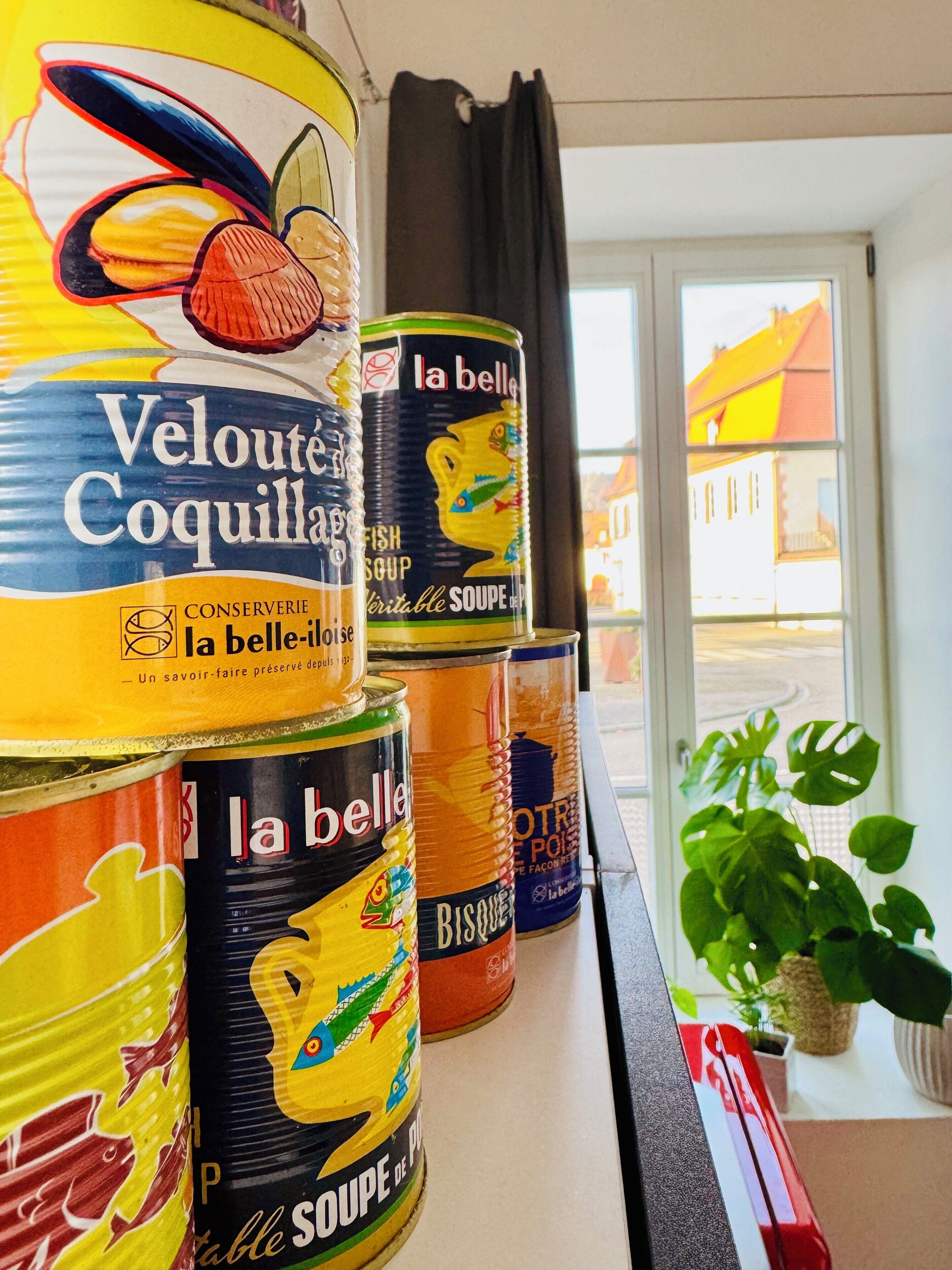 A shelf with various canned goods, including 'Velouté Coquillards' and 'la belle' soup cans.