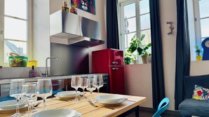 A modern kitchen with a red refrigerator, a dining table set with plates and glasses, and a window with curtains. - Les gîtes de Wissembourg- Color Lodge (Wissembourg)