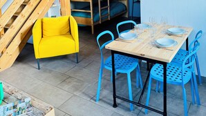 A cozy room with a wooden bunk bed, a yellow chair, a dining table with blue chairs, and a small wooden table with magazines. - Les gîtes de Wissembourg- Color Lodge (Wissembourg)