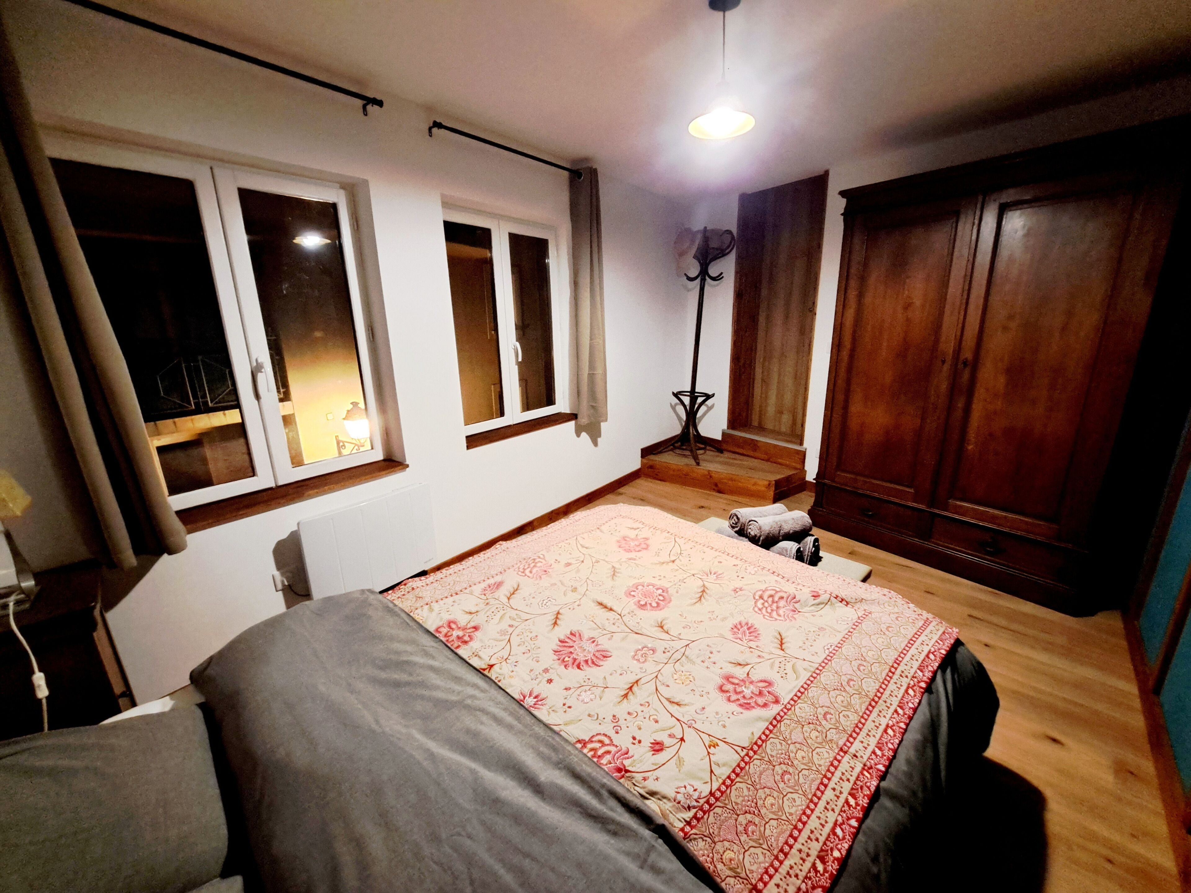 Ein Schlafzimmer mit Bett, Kleiderschrank, Heizkörper und einem fenster mit Vorhängen.