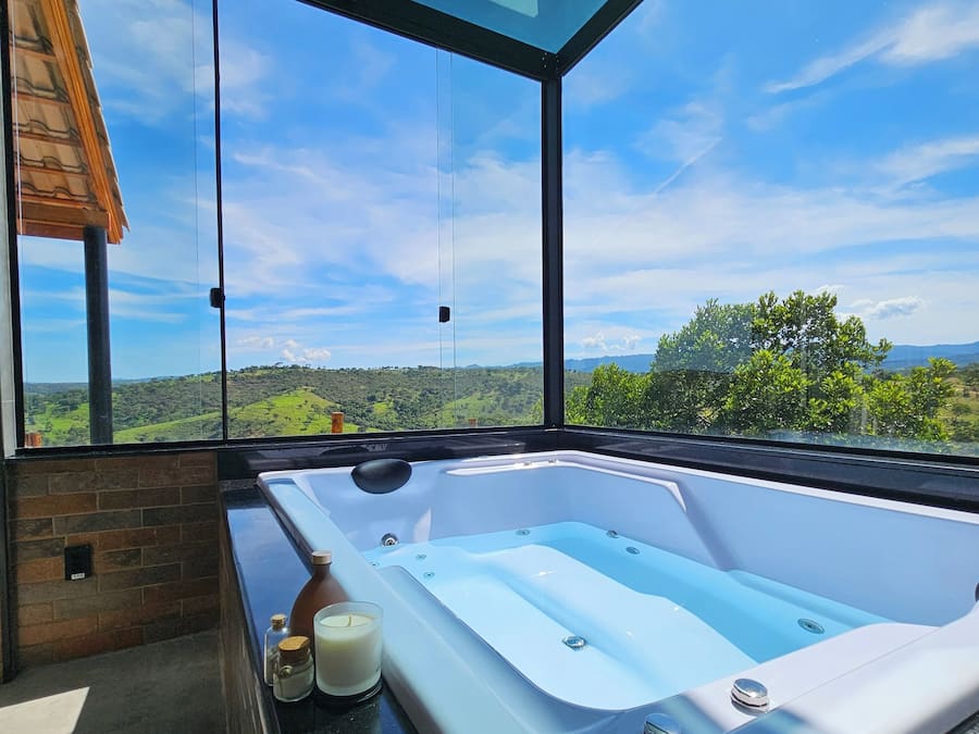 A modern bathroom with a glass-enclosed jacuzzi, a brick wall, and a view of a green landscape.