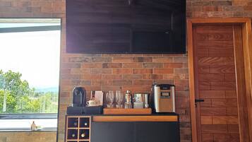 A modern kitchen with a brick wall, a large flat-screen TV, a wine rack, and a coffee machine.