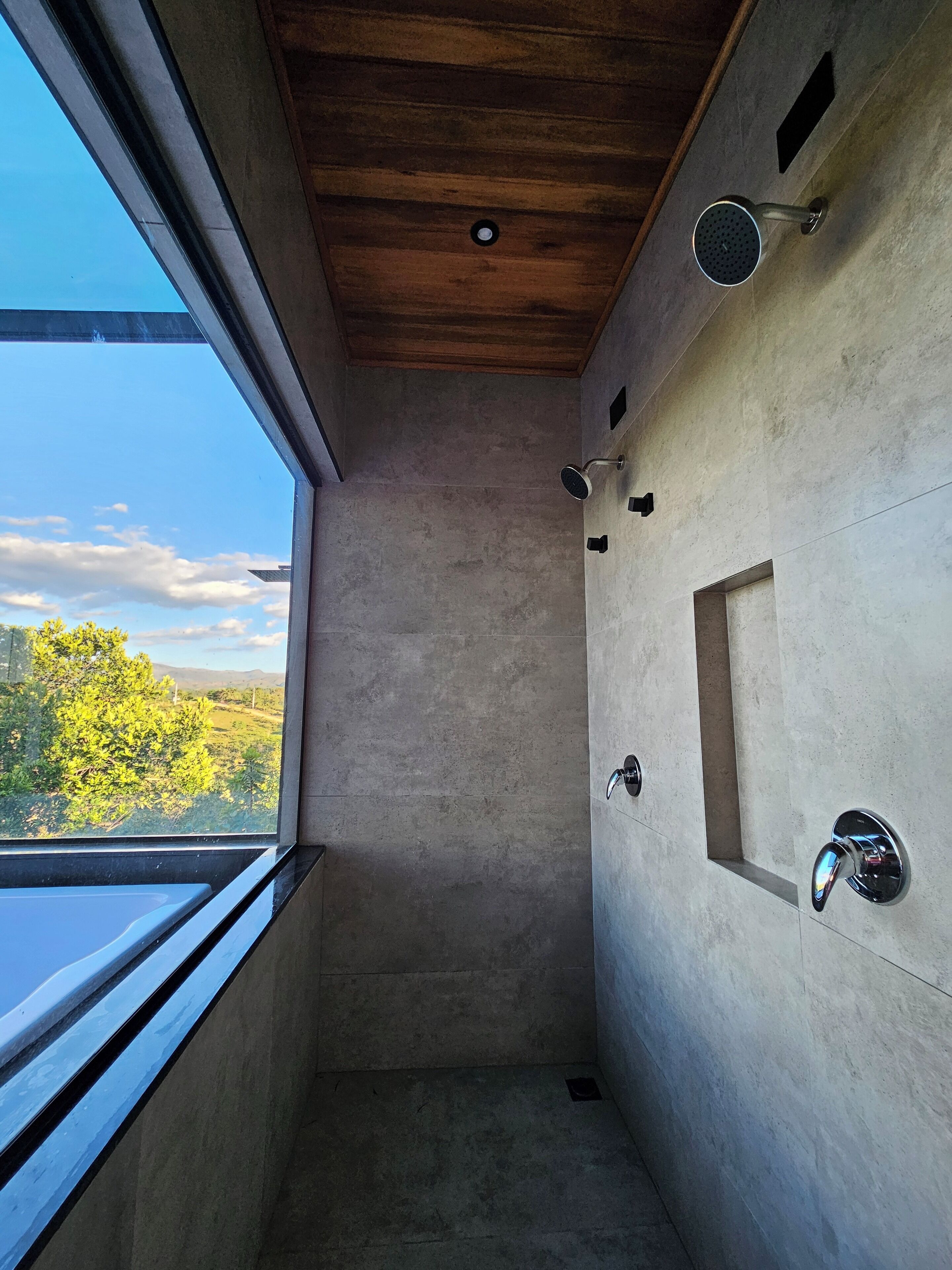 Une douche moderne avec un puits de lumière, un plafond en bois et une vue sur la verdure environnante.