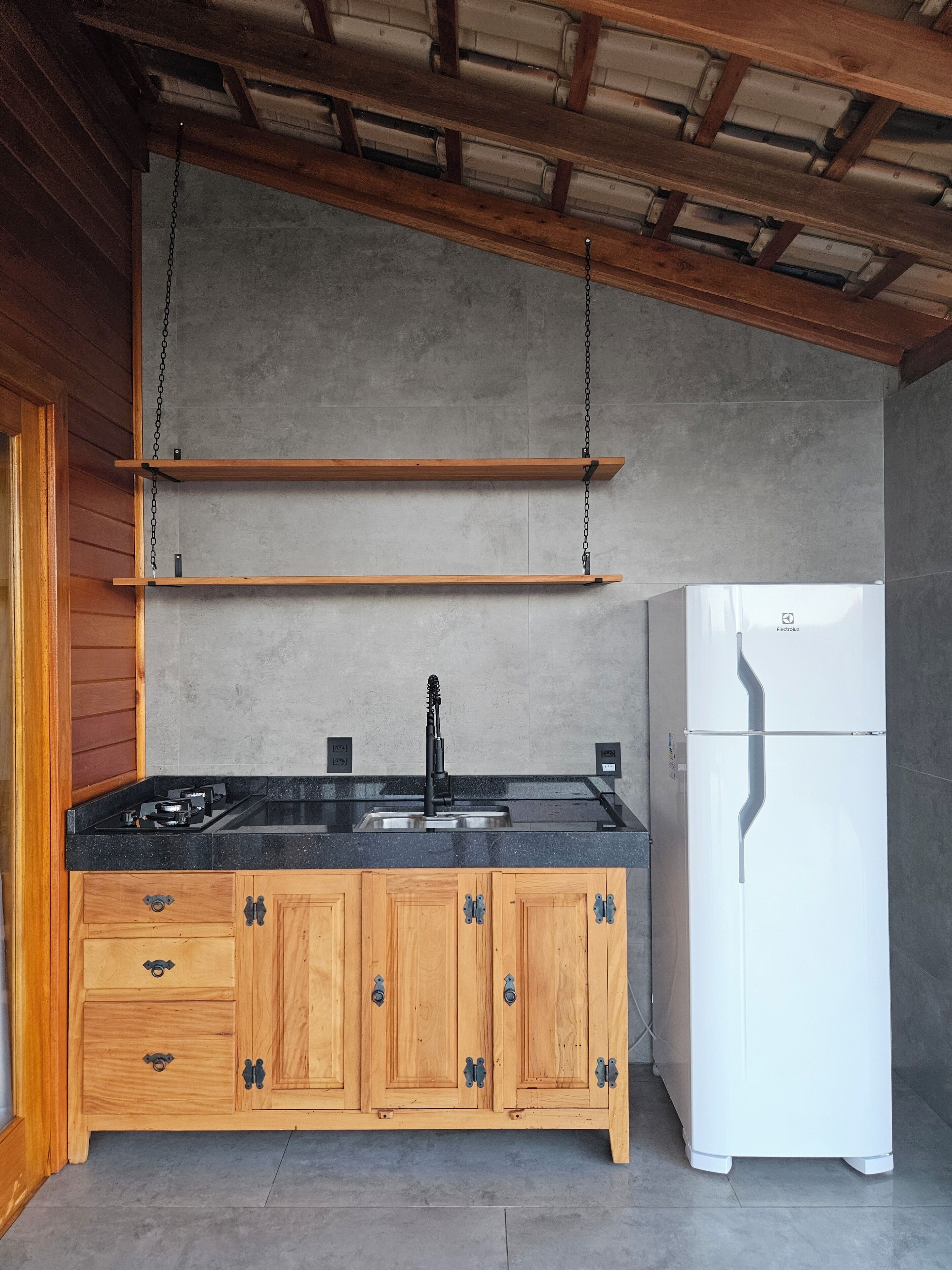 A kitchen with wooden cabinets, a black countertop, a stainless steel sink, and a white refrigerator.