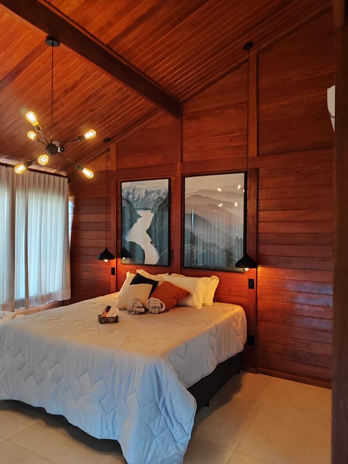 A bedroom with a large bed, wooden walls, a ceiling fan, and two framed pictures.