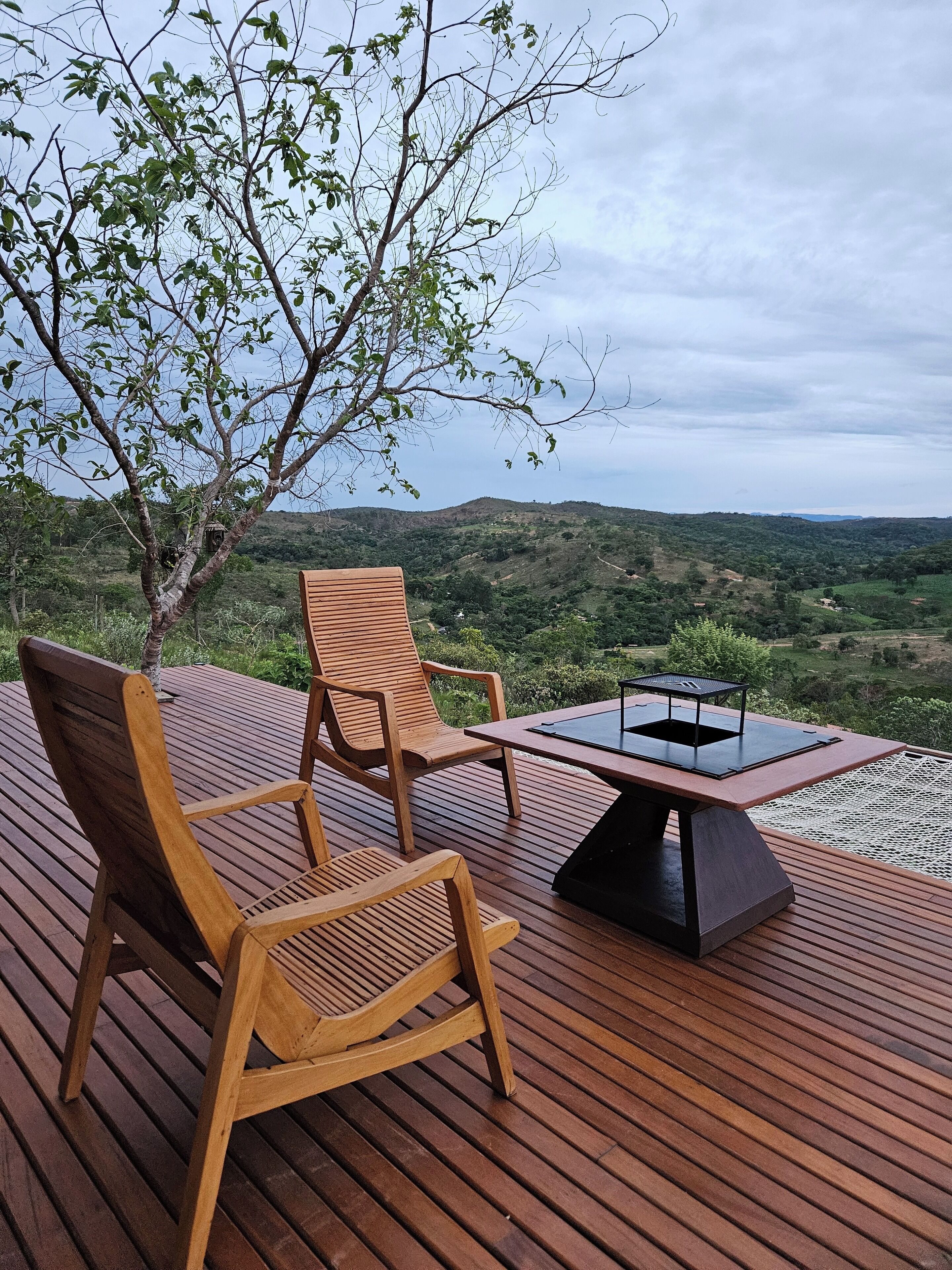 Un terrazzo in legno con due sedie e un tavolo, affacciato su un paesaggio collinare.