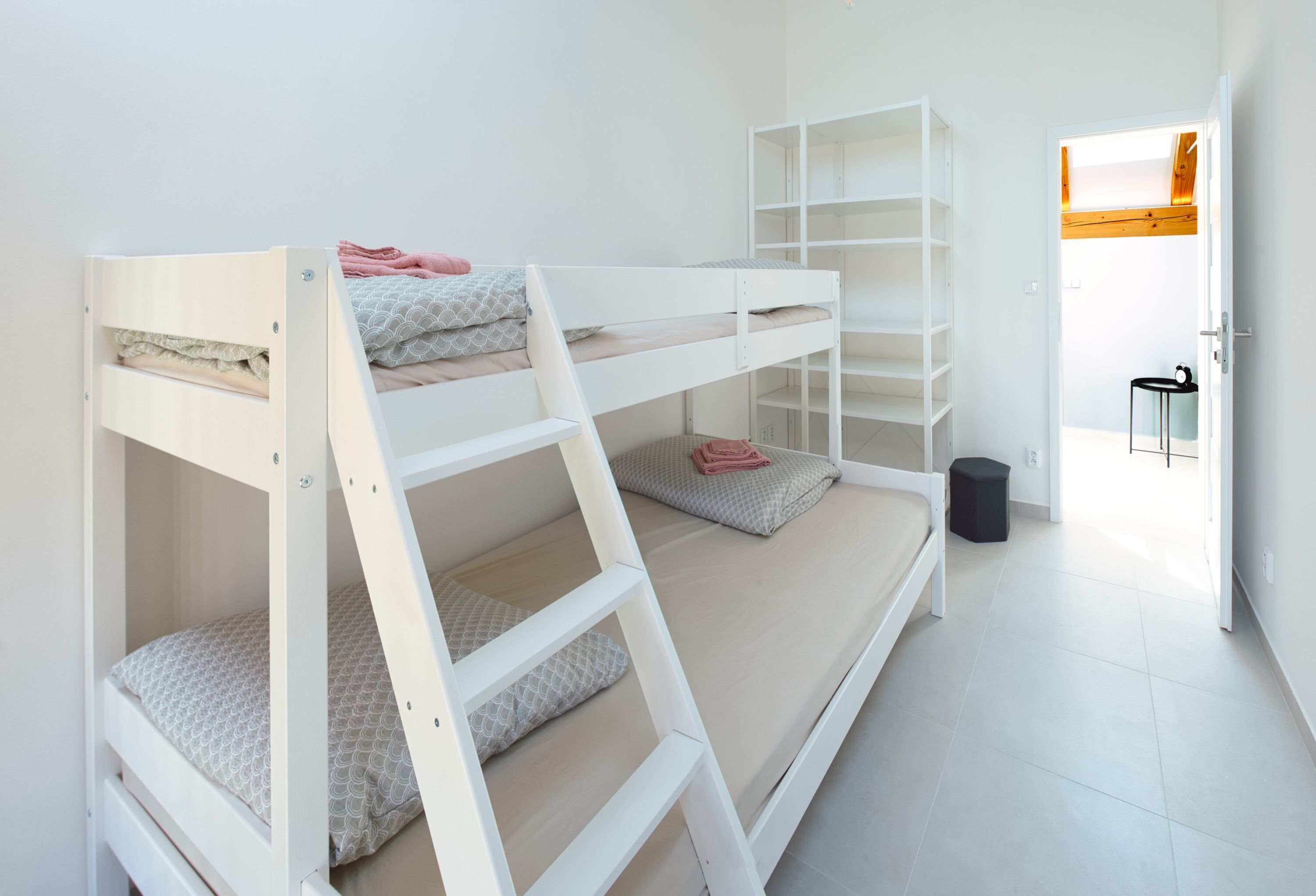Habitación con literas, una escalera, un taburete pequeño y una puerta que da a otra habitación.
