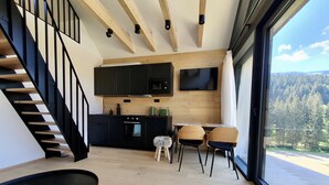 Una cocina moderna con armarios negros, una zona de comedor de madera y un amplio ventanal con vistas a un bosque.