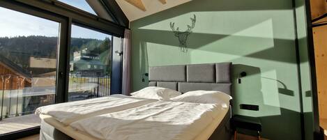 A modern bedroom with a large bed, a view of the outdoors, and a unique ceiling design.