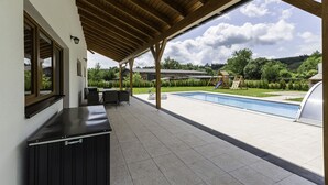 A covered outdoor area with a pool, seating, and a view of a playground. - Prosence Kpa250 in Prosecn (Prosečné)