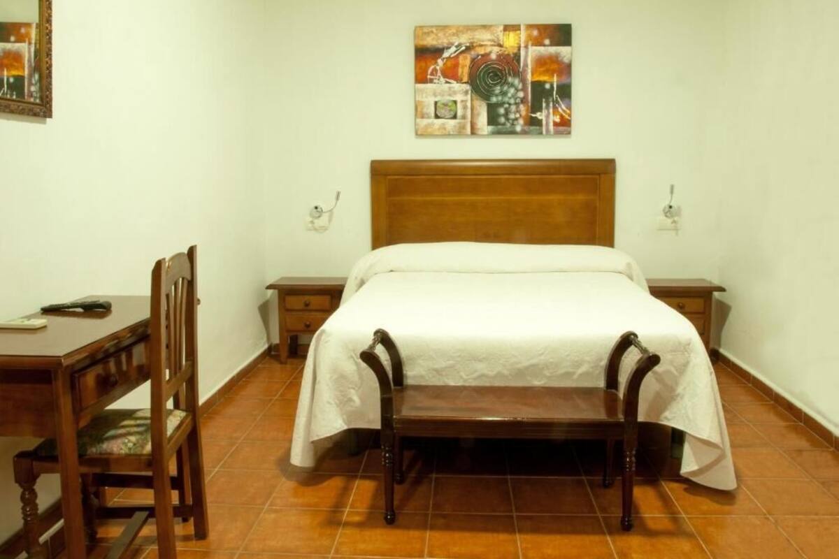Un dormitorio con una cama de madera, un escritorio con silla y un cuadro en la pared.