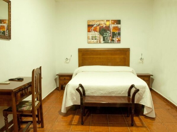 A bedroom with a wooden bed, a desk with a chair, and a painting on the wall. - HOTEL LAS SALINAS  CABO DE GATA (Almeria)