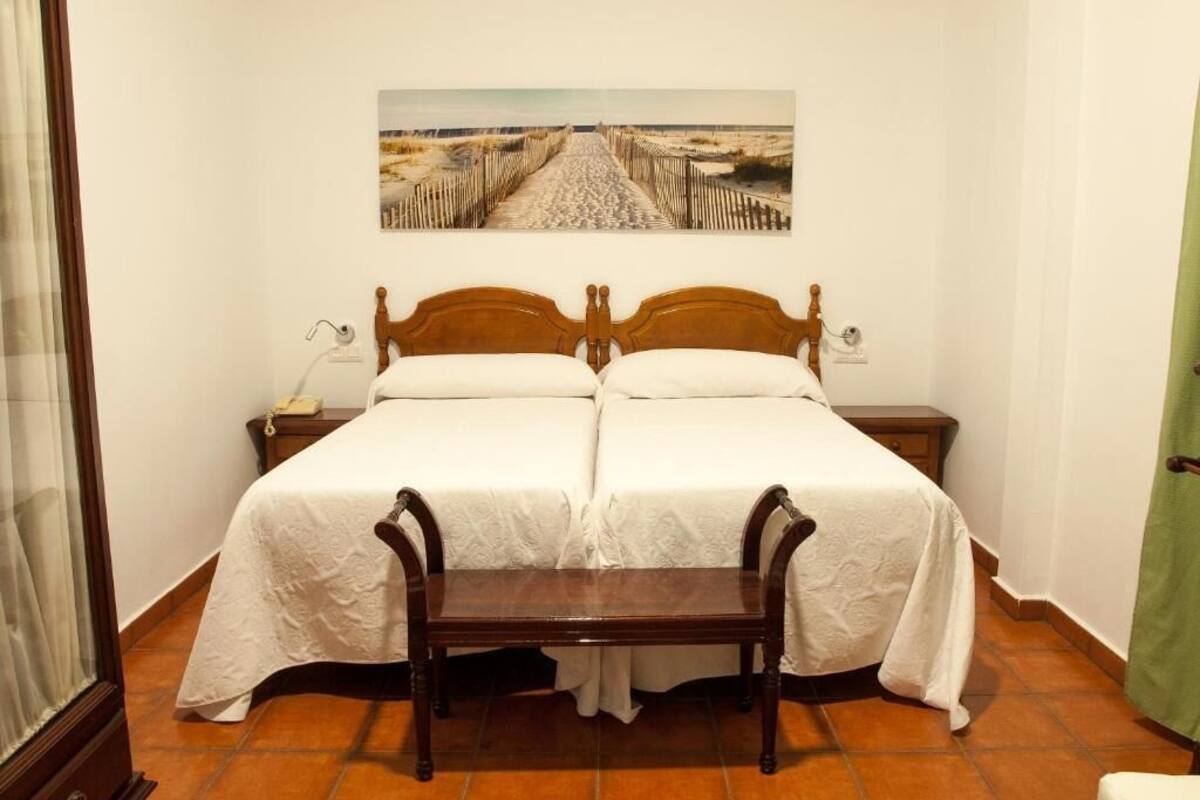 Una cama doble con cabecera de madera, una mesita de noche con lámpara y un cuadro con una escena de playa sobre la cama.