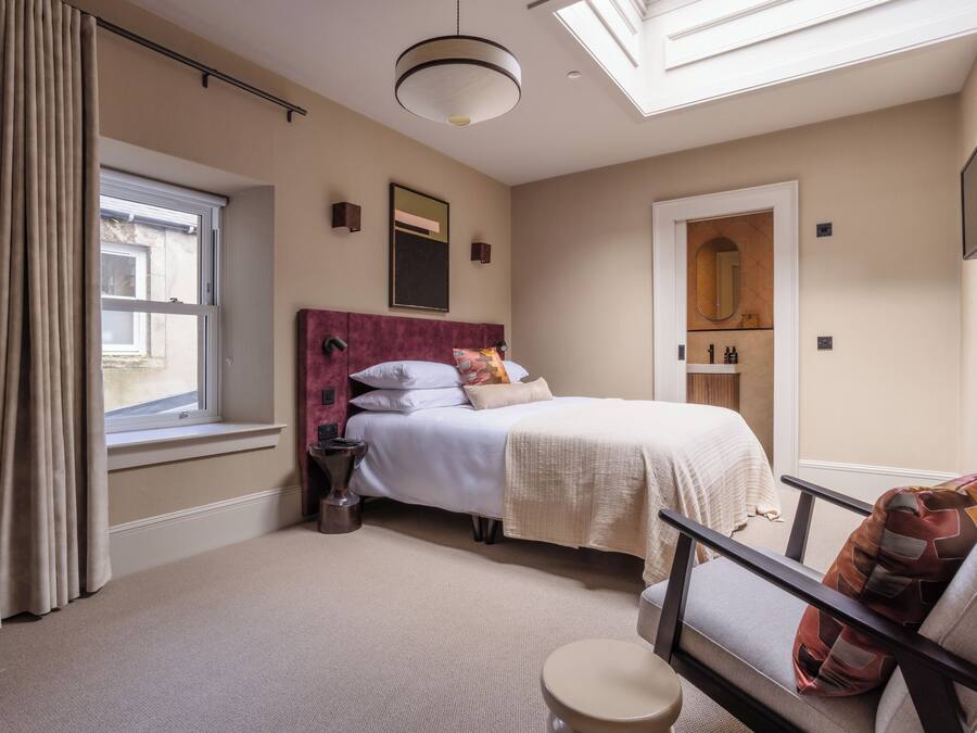 A bedroom with a bed, a chair, a bedside table, a mirror, and a window.
