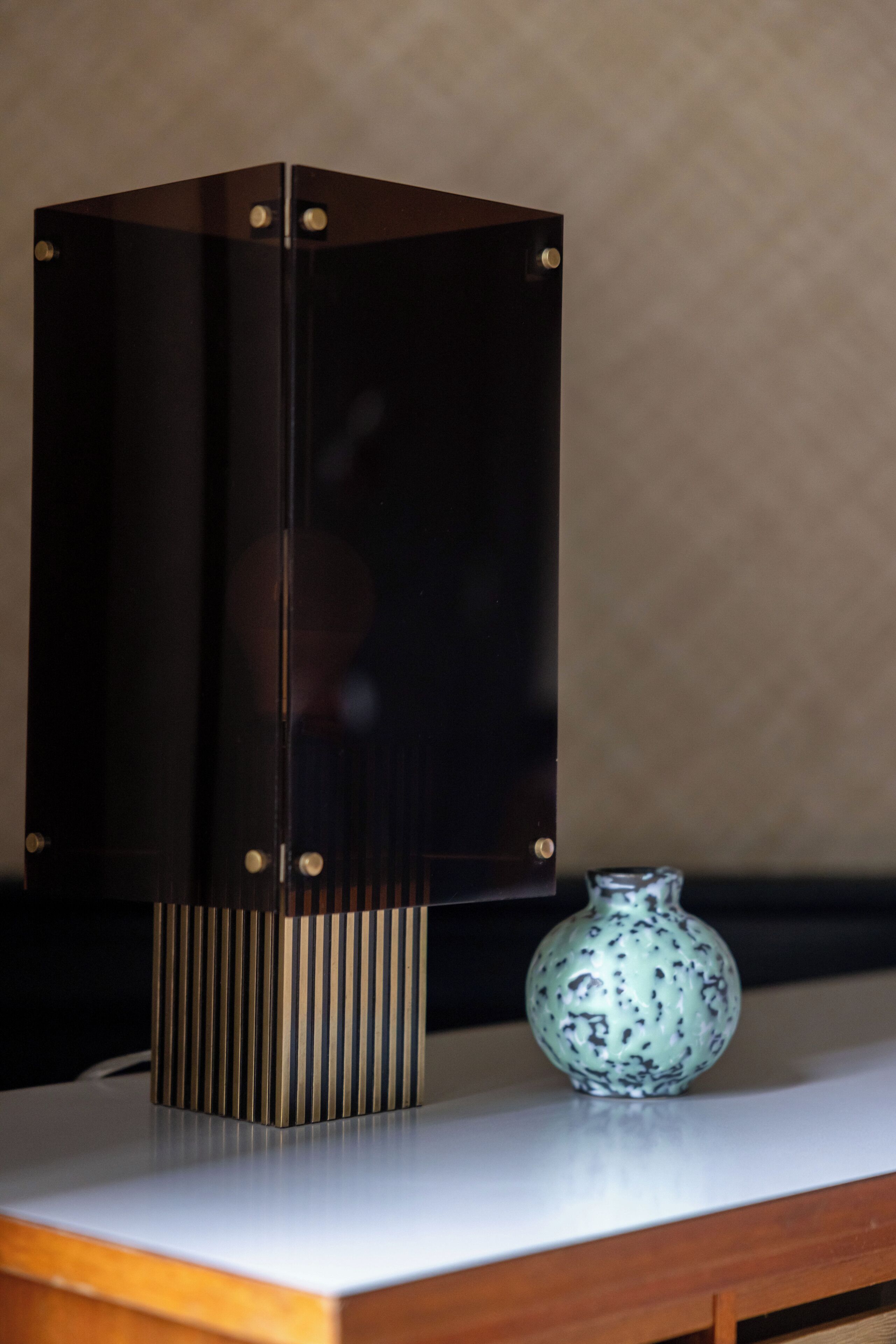 A modern, dark-colored cabinet with a textured base, a small, speckled vase, and a white countertop.