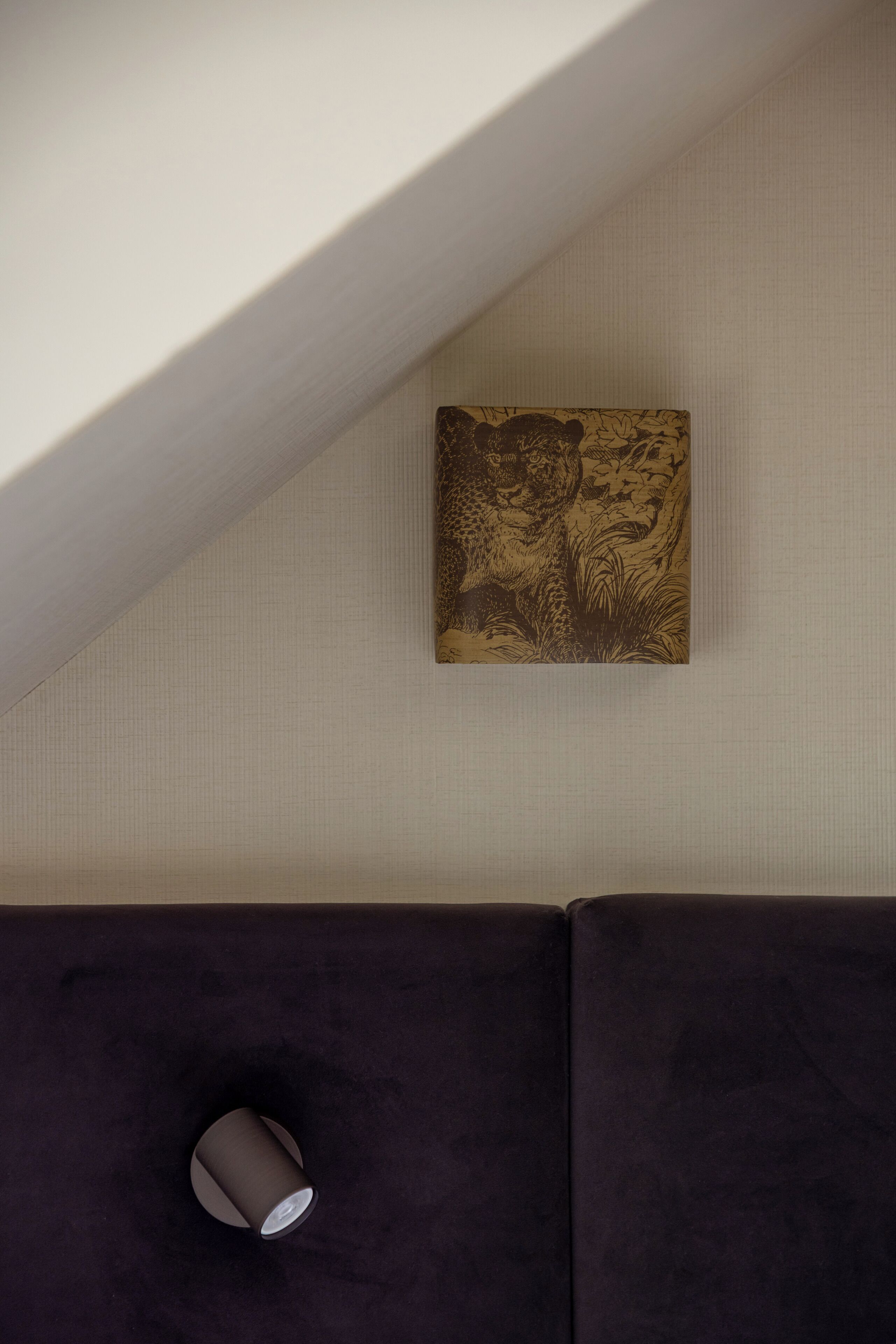 Ett rum med en soffa i mörk färg, en liten, rund lampa och ett konstverk som hänger på väggen och föreställer en leopard.