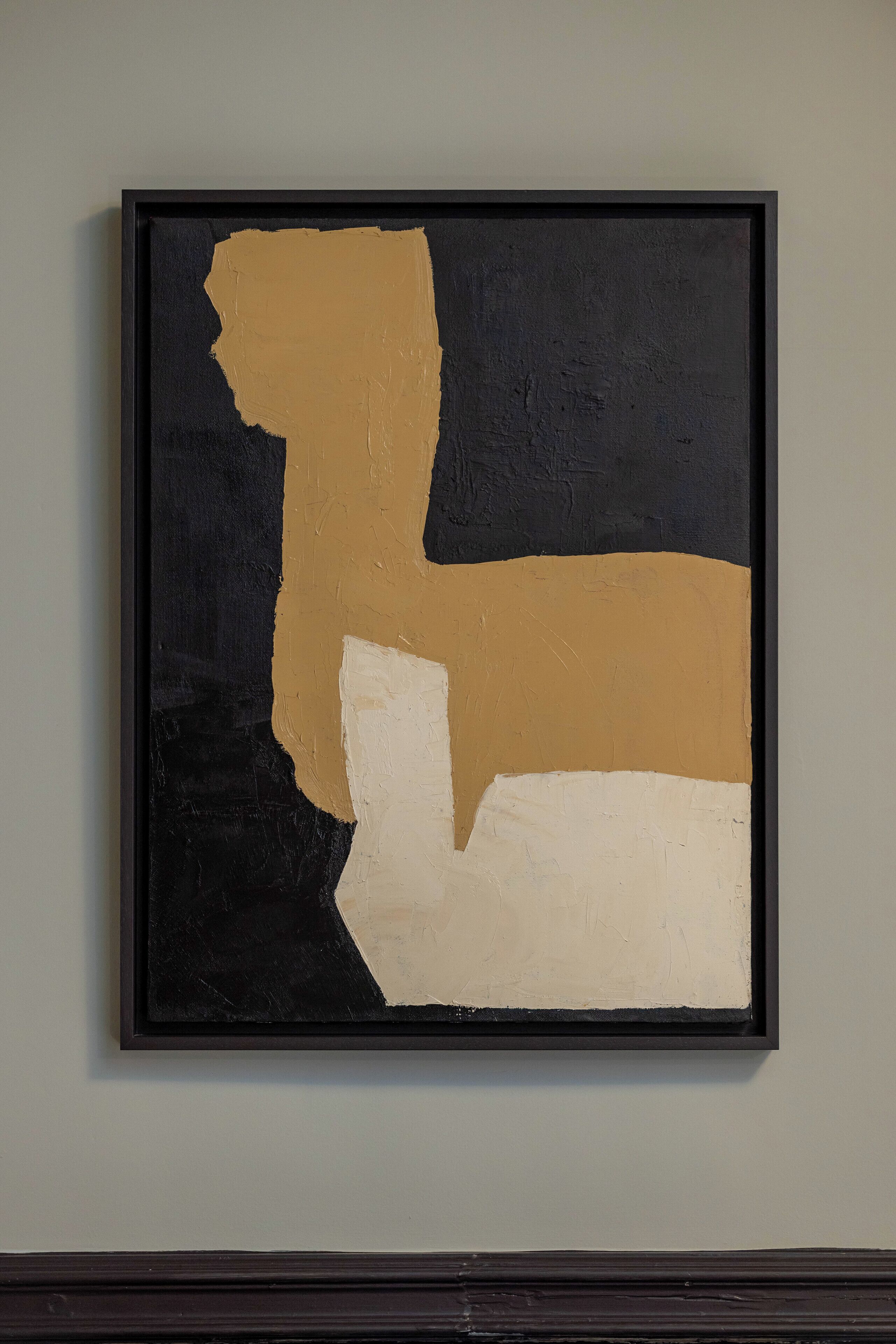 A framed abstract painting with black, beige, and white sections on a plain wall.