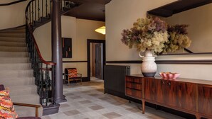 A staircase with a wooden handrail, a large vase with dried flowers, and a wooden console table with a pink bowl on top. - 3 Johns Place Townhouse (Edinburgh)