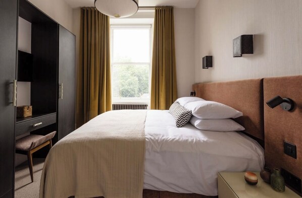 A hotel room with a bed, bedside table, lamp, and a window with curtains.