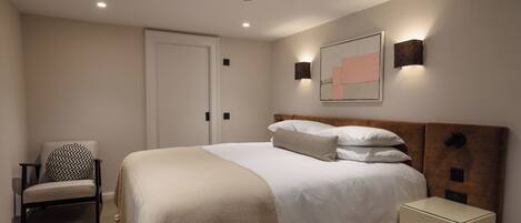 A neatly arranged bedroom with a large bed, a chair, a bedside table, and a door.