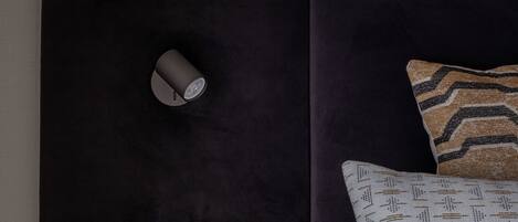 A bedroom with a dark headboard, a bedside table with a vase, and a wall-mounted light fixture.