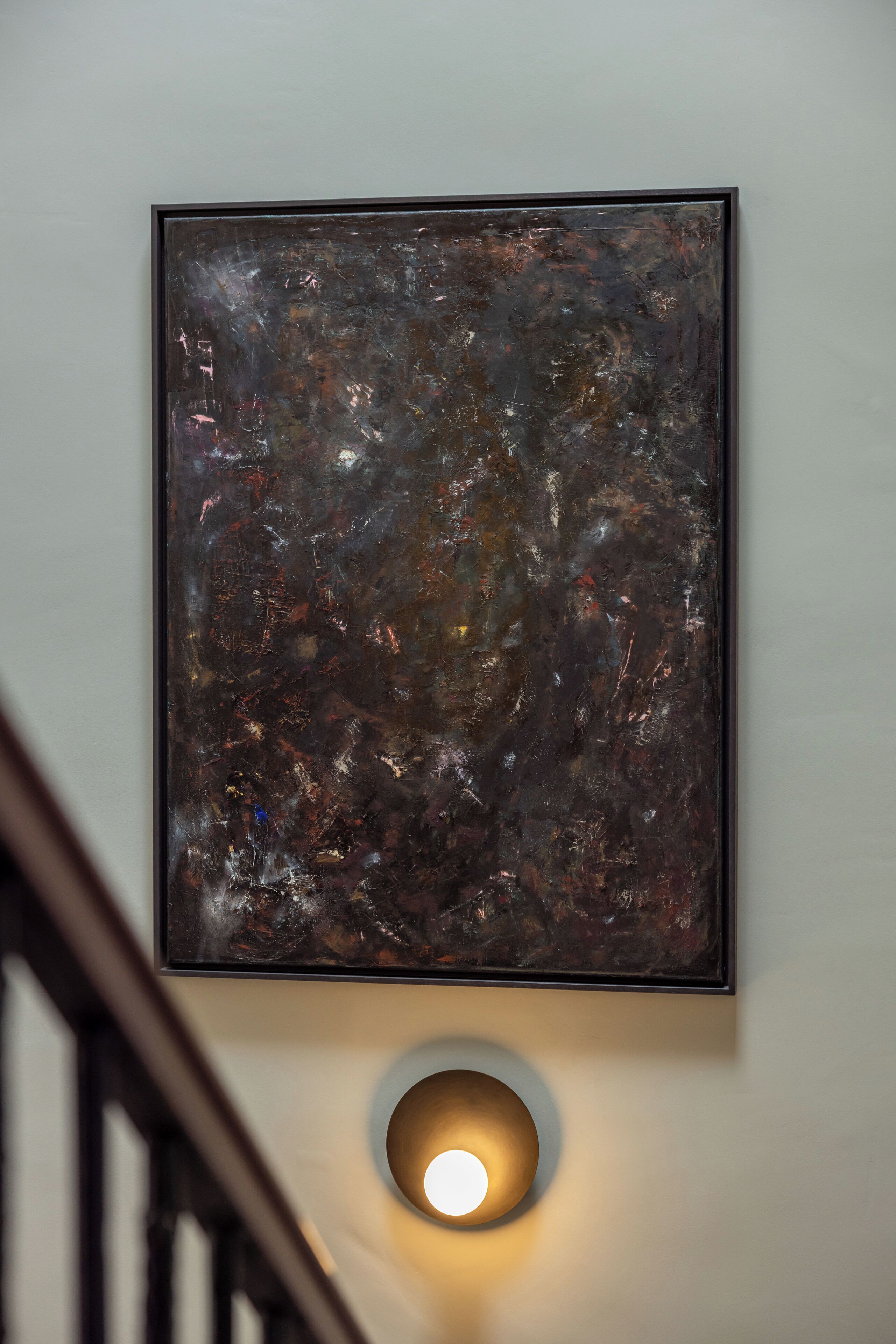 A framed abstract painting on a wall with a round light fixture below it.