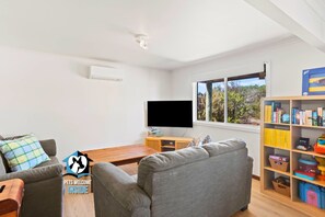 A modern living room with a grey sofa, a wooden coffee table, a flat-screen TV, and a bookshelf filled with books and toys.