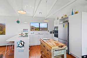A modern kitchen with white cabinetry, a wooden island, and a large window overlooking a scenic view.