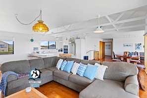 A spacious living area with a grey sectional sofa, wooden dining table, and pendant lighting.