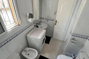 A compact bathroom with a washing machine, a sink, and a bidet. - Sunset View Golf Course Apartment Alicante (Rojales)