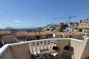 A balcony with a view of a residential area, including houses with red-tiled roofs and a construction crane in the distance. - Sunset View Golf Course Apartment Alicante (Rojales)