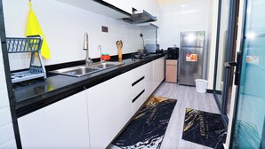 A modern kitchen with white cabinets, black countertops, stainless steel appliances, and a black and gold marble backsplash. - Staroot Residences (Nairobi)