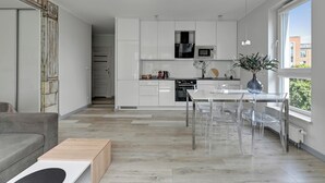A modern kitchen with white cabinets, a dining area with clear chairs, and a large window providing natural light. -  Bastion Wałowa City Center & Parking by Downtown Apartments (Gdansk)